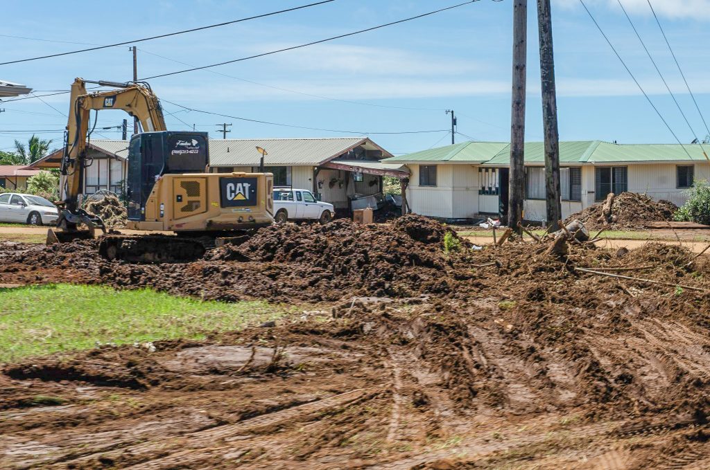 Neighbor operates an excavator on Kamakani Dancil's property on Niu Street in Nā‘ālehu on Aug. 19, 2026, to clear mud and debris left behind by Hurricane Lala. (Tiffany DeMasters/Big Island Now)