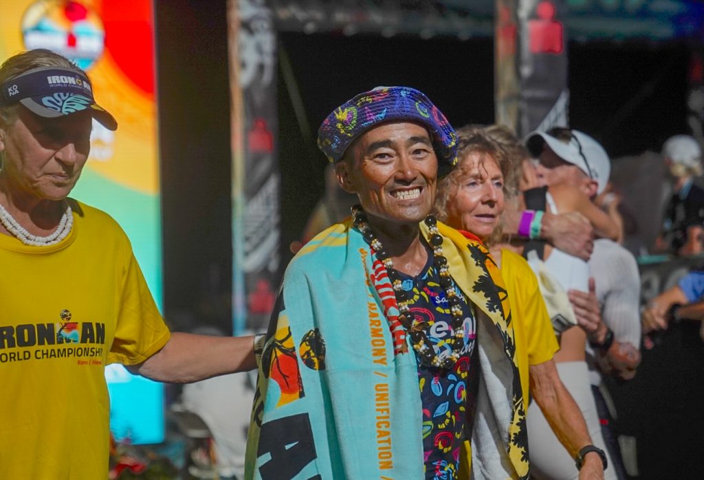 Keish Doi of Kailua-Kona was draped in an towel after crossing the finish line at the Ironman World Championship in Kona on Oct. 10, 2026. (Tiffany DeMasters/Big Island Now)